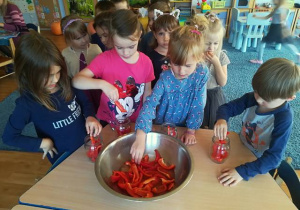 Grupa dzieci wkłada paprykę do słoików.